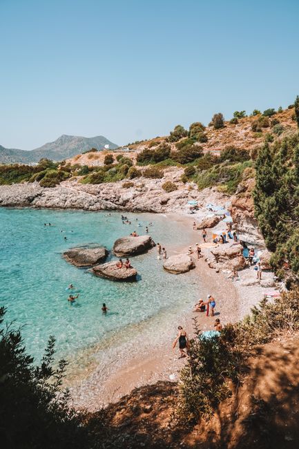 A vibrant summer day at a rocky beach in Muğla, Turkey, with people enjoying the clear waters.