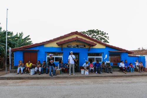 Free Group of people sitting and standing by a blue building on a street in daylight. Stock Photo