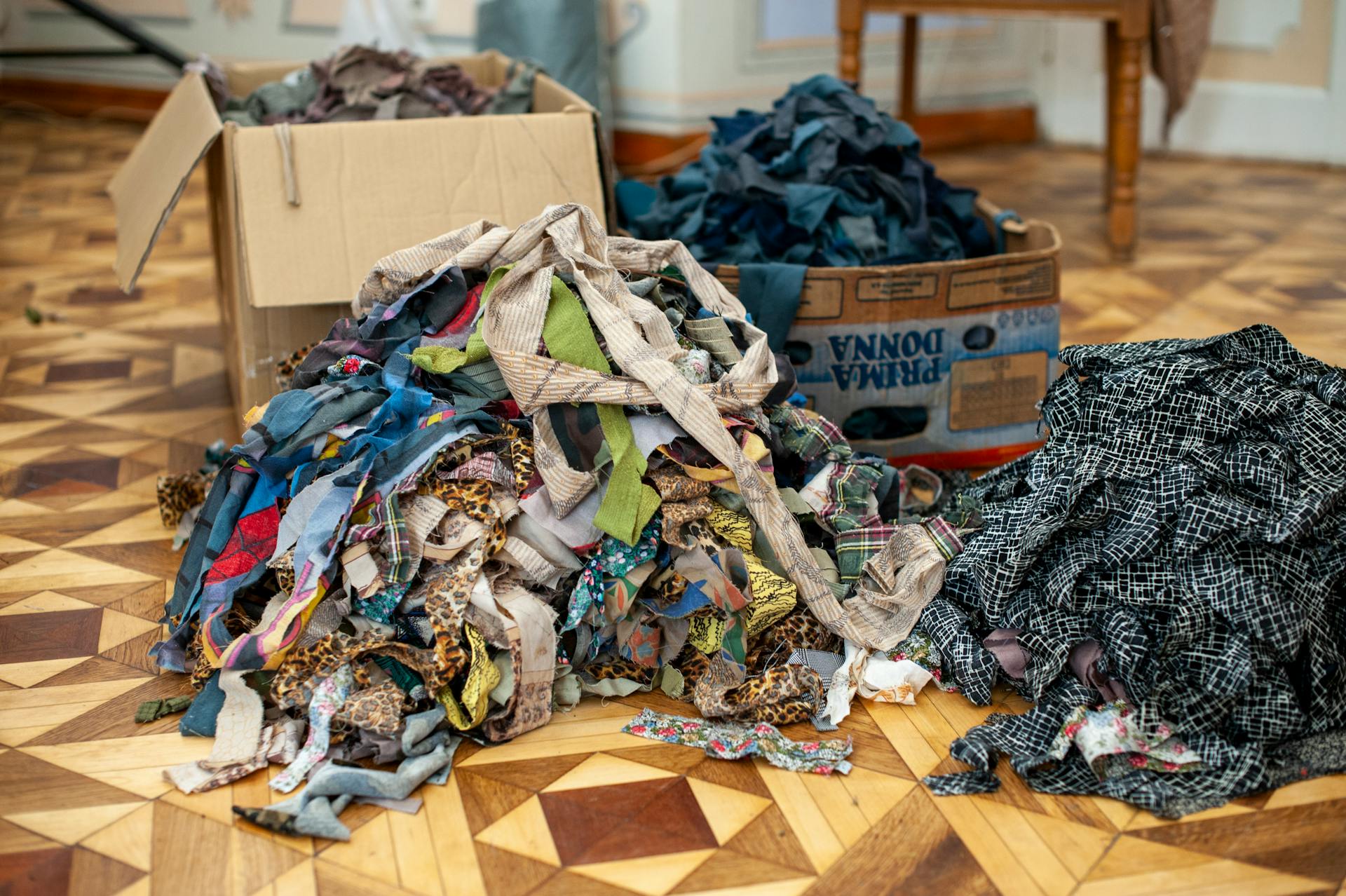 A pile of colorful shredded fabric scraps on a wooden patterned floor indoors.