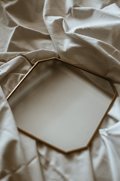 Square Mirror Lying on White Sheet