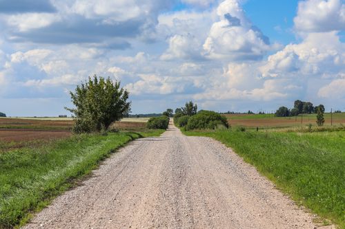 Free Scenic view of a gravel road through lush farmlands and fields under a blue sky in Poland. Stock Photo