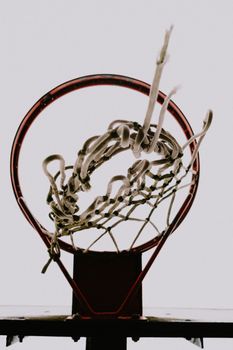 Close-up image of a worn-out basketball hoop with a broken net against a neutral sky.