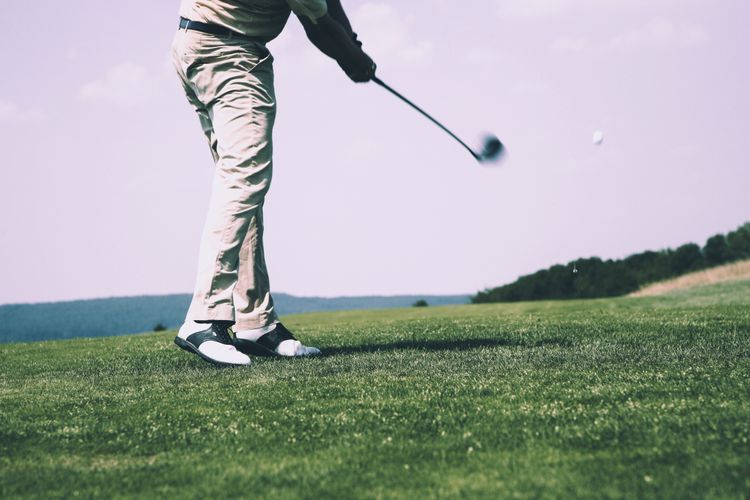 A golfer completes a full driver swing on a wide-open fairway under a bright sky, demonstrating a controlled tee shot with good extension through impact.