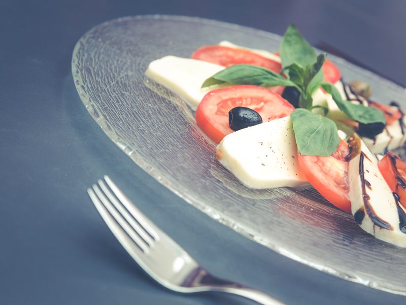 A fresh Caprese salad with tomatoes, mozzarella, basil, and olives on a glass plate.
