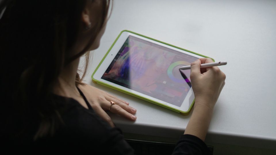 A woman uses a stylus pen on a tablet computer, creating digital art.