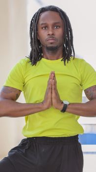 An adult man in a yellow shirt practicing yoga indoors with praying hands.