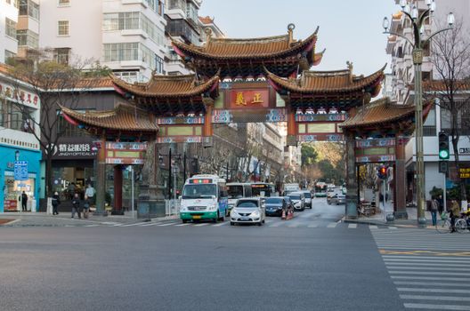 A bustling street scene in Kunming with a traditional Chinese gate and modern cityscape.