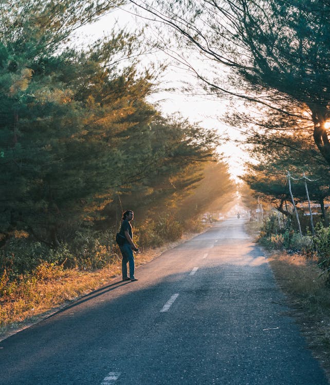 Man Wearing Black Shirt and Blue Pants on Side of Asphalt Road