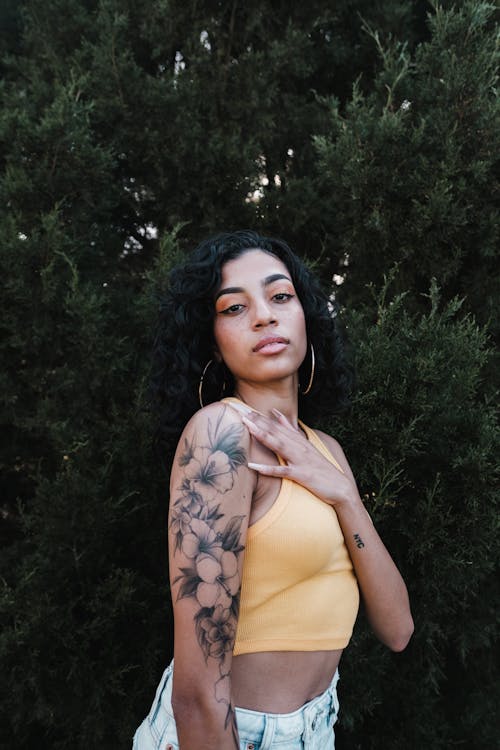 Woman in Yellow Crop Top Standing Beside Green Plant