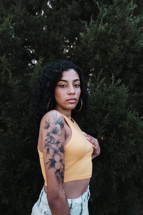 Woman in Yellow Crop Top Standing Beside Green Leaves