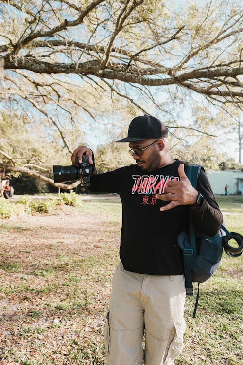 Man Wearing Black Shirt and Black Cap Holding a Camera
