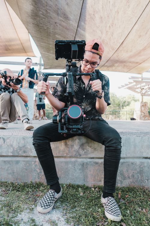 Free A male videographer sitting outdoors, handling a professional camera setup on a gimbal. Stock Photo