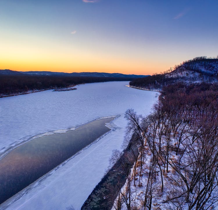 View Of Wide Frozen River With Forested River Banks