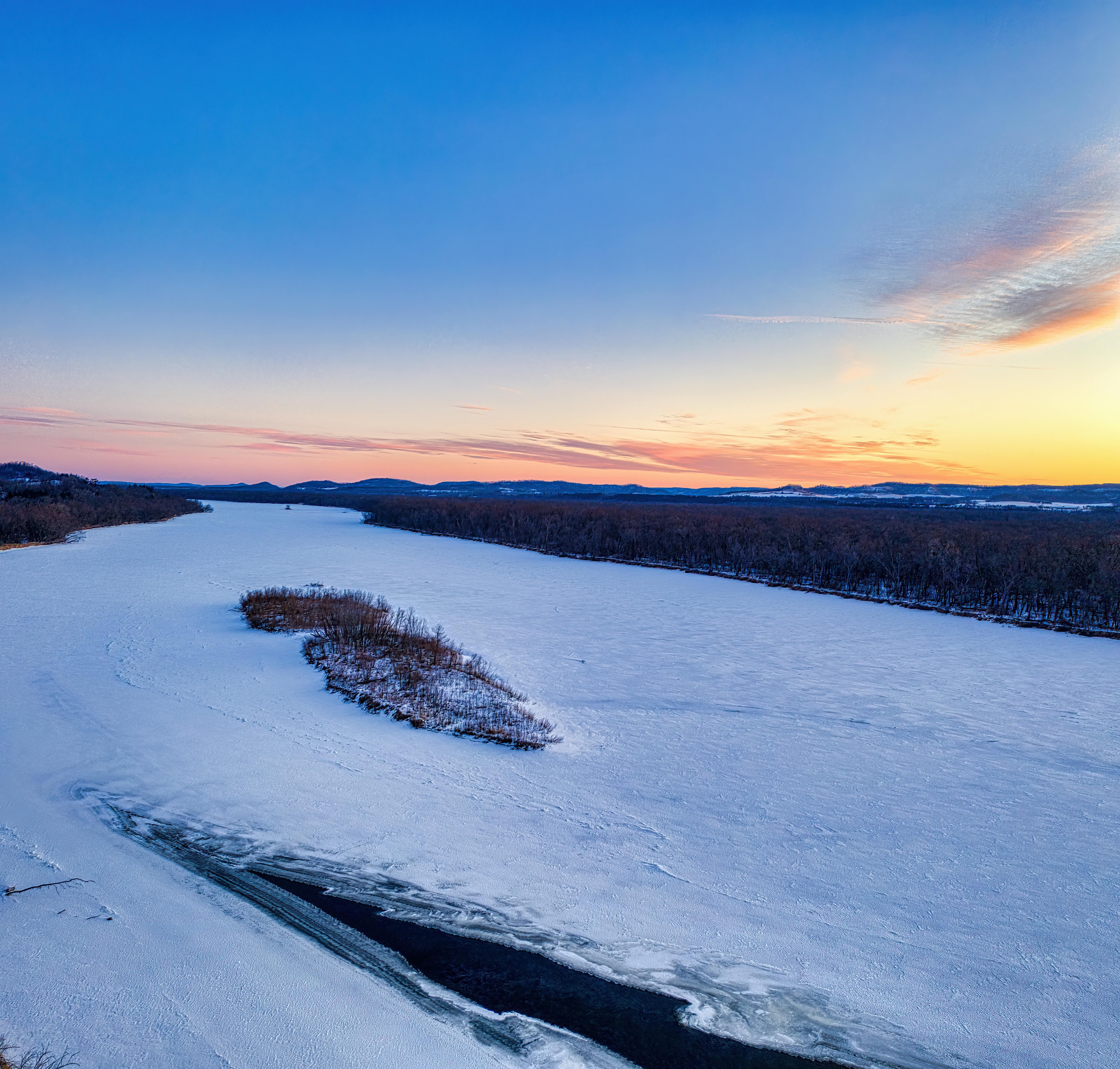 Aerial view of a frozen river with a stunning winter sunset sky in Ella, WI.