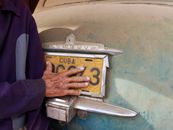 Hand of Elderly Man Touching Licence Plate on Car