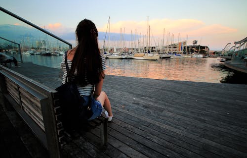 黑色和白色的條紋勺脖子襯衫的女人在白天坐在船塢的棕色木凳上