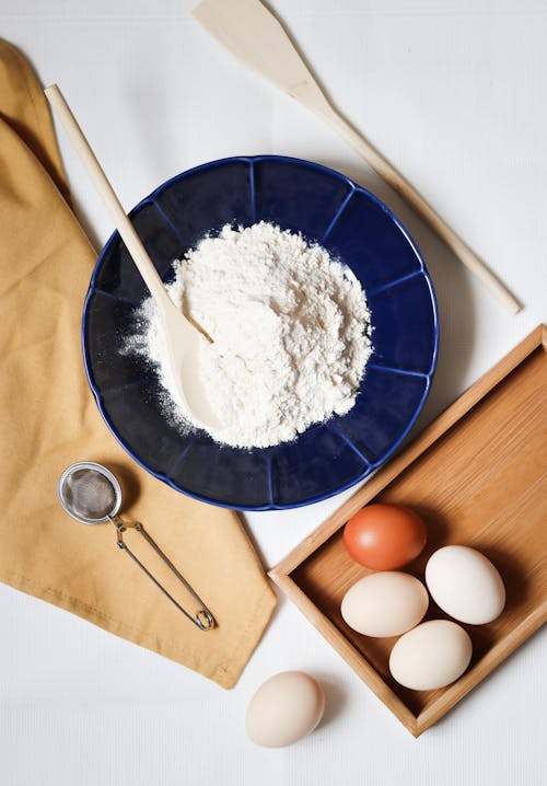 Flour on a Blue Ceramic Plate and Eggs on a Wooden Tray