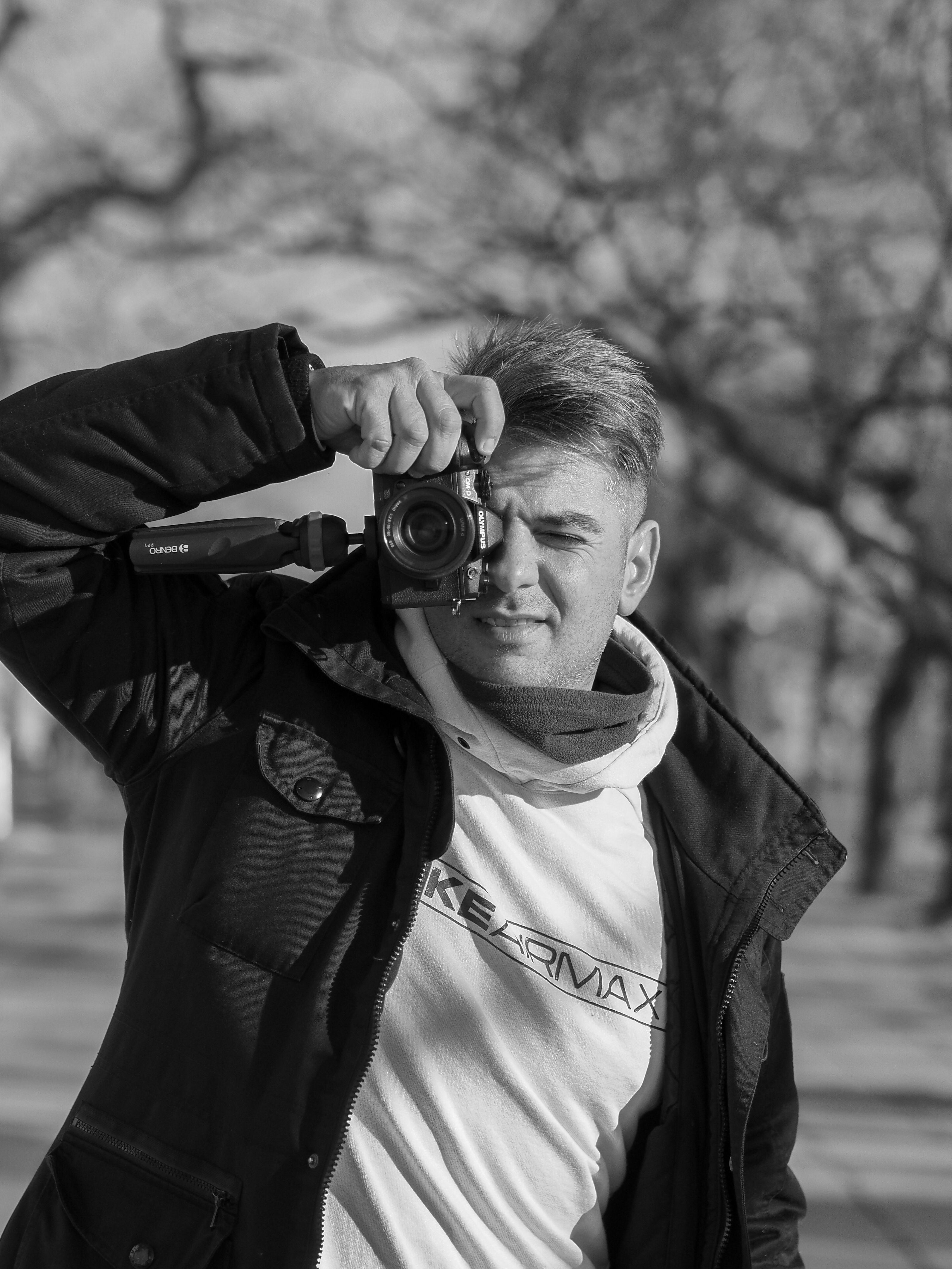 Black and white photo of a male photographer holding a camera outdoors.