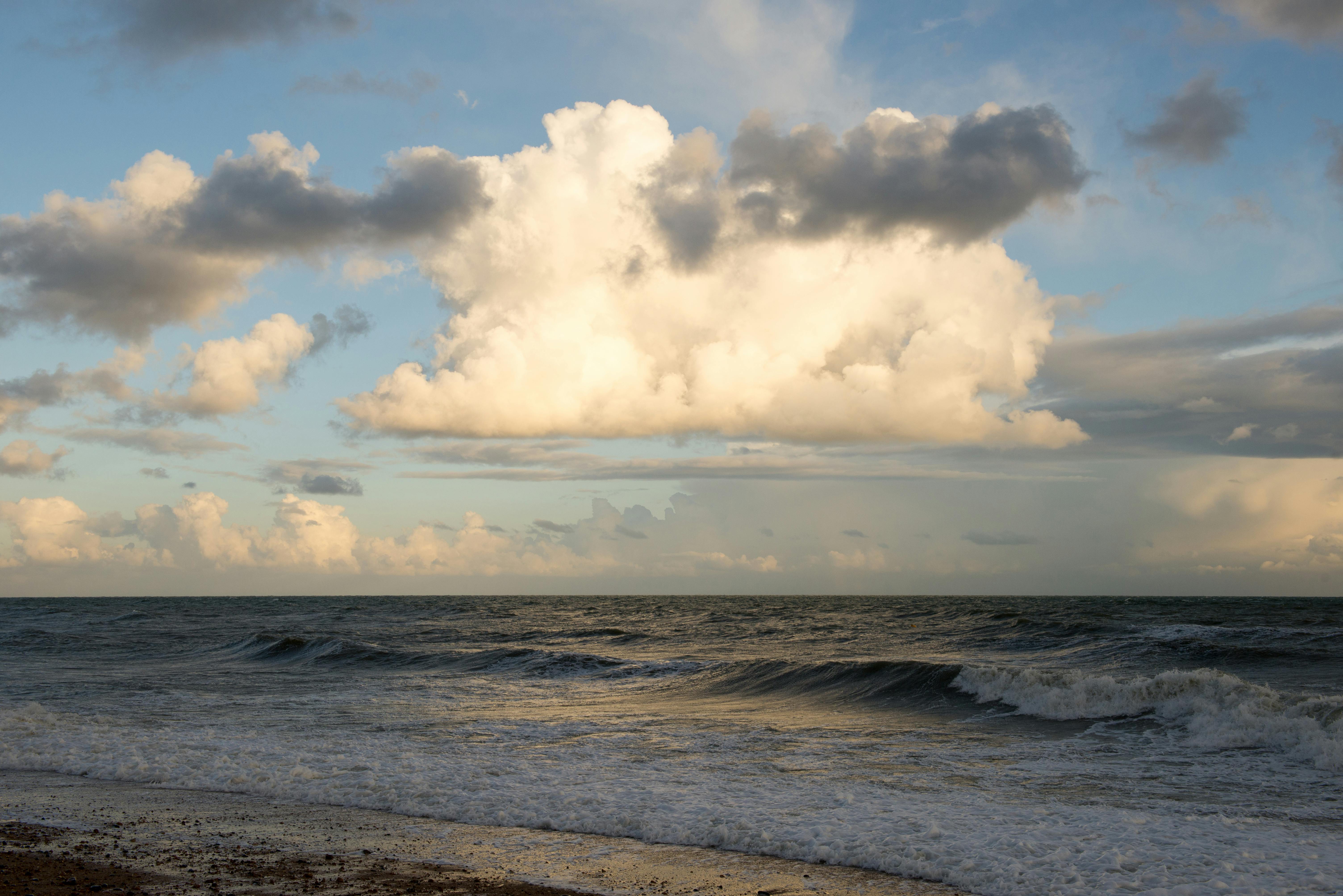 ocean waves crashing on shore under white clouds and blue sky