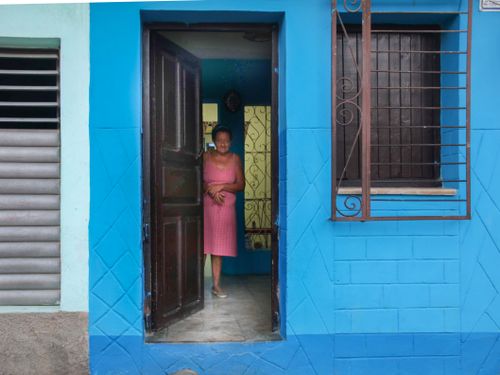 Free A woman stands smiling in a brightly painted blue entranceway, conveying warmth and hospitality. Stock Photo