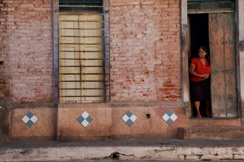 Woman in Red Dress Standing Beside a Front Door
