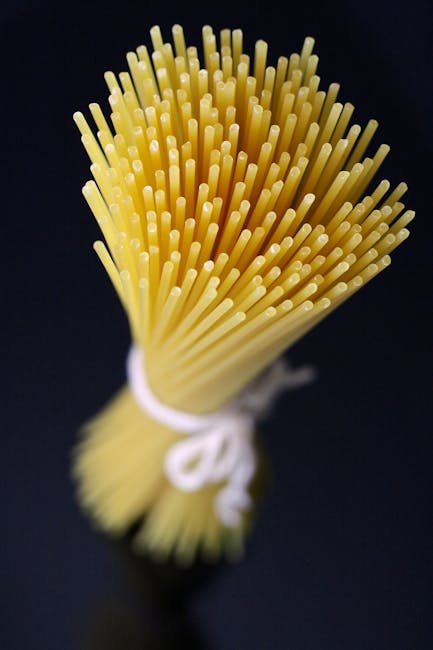 A bundle of dried spaghetti strands standing upright next to a cooked portion twirled on a fork with tomato sauce.