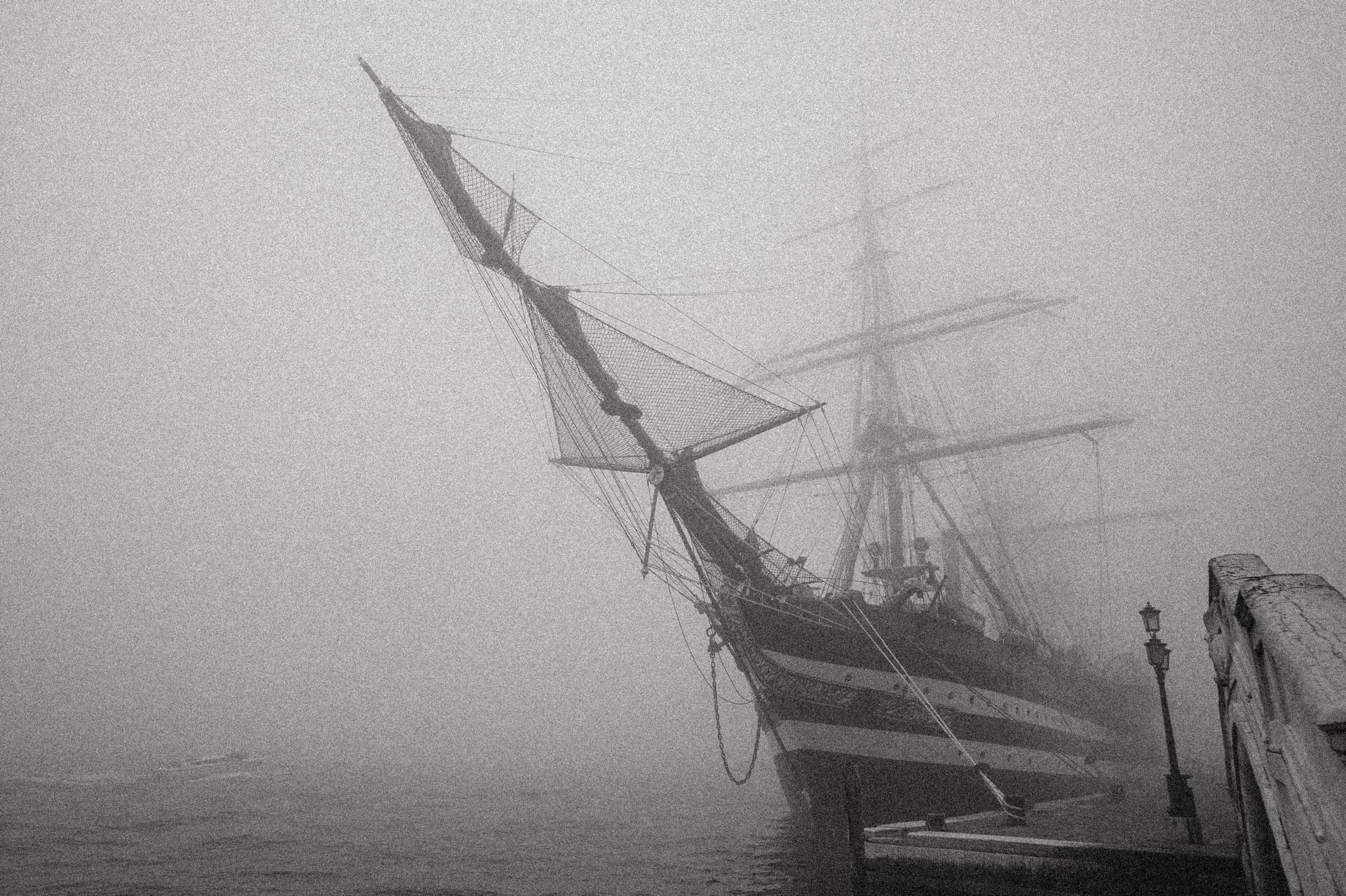 A monochrome portrayal of a historic ship docked in a foggy harbor, evoking a sense of mystery.