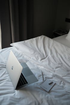 Laptop and notebook on a bed, perfect for remote work setup inspiration.