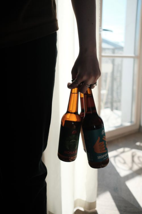 Free A person holding two beer bottles in a silhouette setting indoors with natural window light. Stock Photo