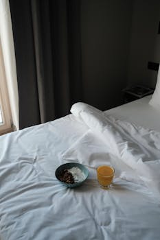 A serene morning setting with muesli and orange juice on a neatly made bed.