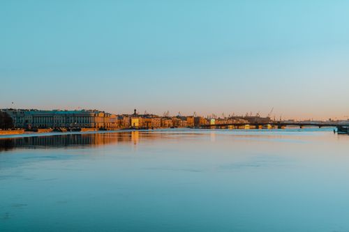 Free Cityscape view of buildings and bridge by the river at sunset, reflecting light on calm water. Stock Photo