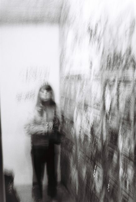 Blurry image of a person standing near a wall covered with posters, creating a surreal motion effect.