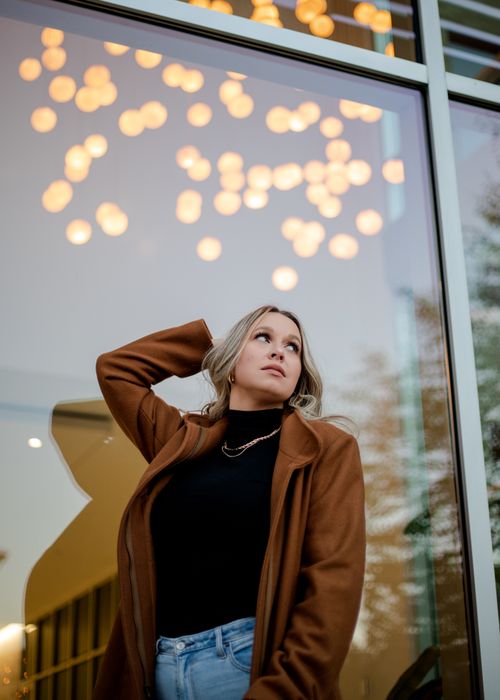 Free Stylish woman in coat posing near glowing cafe lights, looking up thoughtfully. Stock Photo