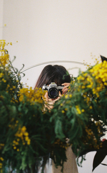Photographer capturing a reflective floral scene with camera, behind a vibrant bouquet.