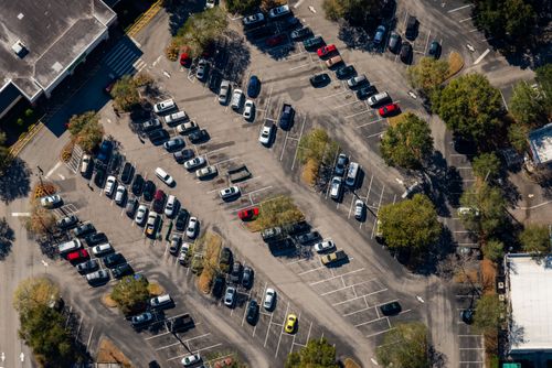 Free Aerial view of a busy parking lot in Florida with parked cars and surrounding trees. Stock Photo