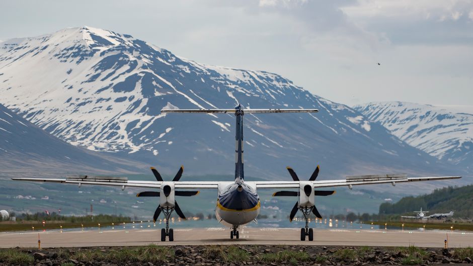 Commercial aircraft on the runway in Akureyri, Iceland, with snowy mountains in the background.