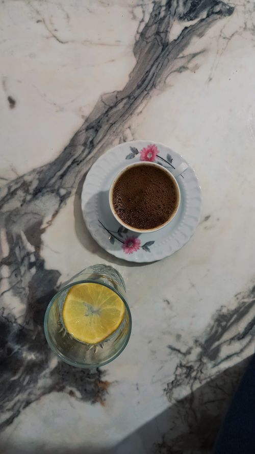 Free Top view of a floral cup of coffee and lemon water on marble surface, offering a cozy vibe. Stock Photo
