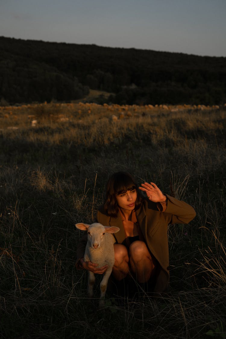 Young Woman Holding White Lamb In Pasture