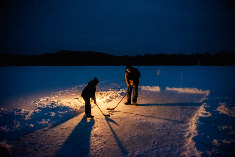 Man And Child Playing Hockey On Snow-Covered Ground