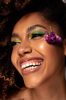 Close-up portrait of a smiling woman with stunning art makeup and purple flower in her afro hair.