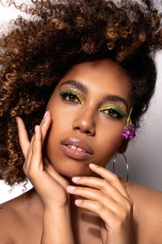 Close-up portrait of a woman with vibrant green eye makeup and curly hair, exuding elegance and style.