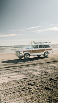 Retro SUV carrying surfboards on a scenic sandy beach with ocean waves and clear sky.