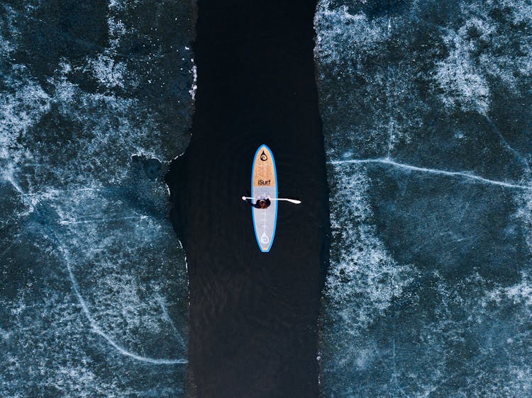 Aerial View Of Man Paddleboarding Through Frozen Lake