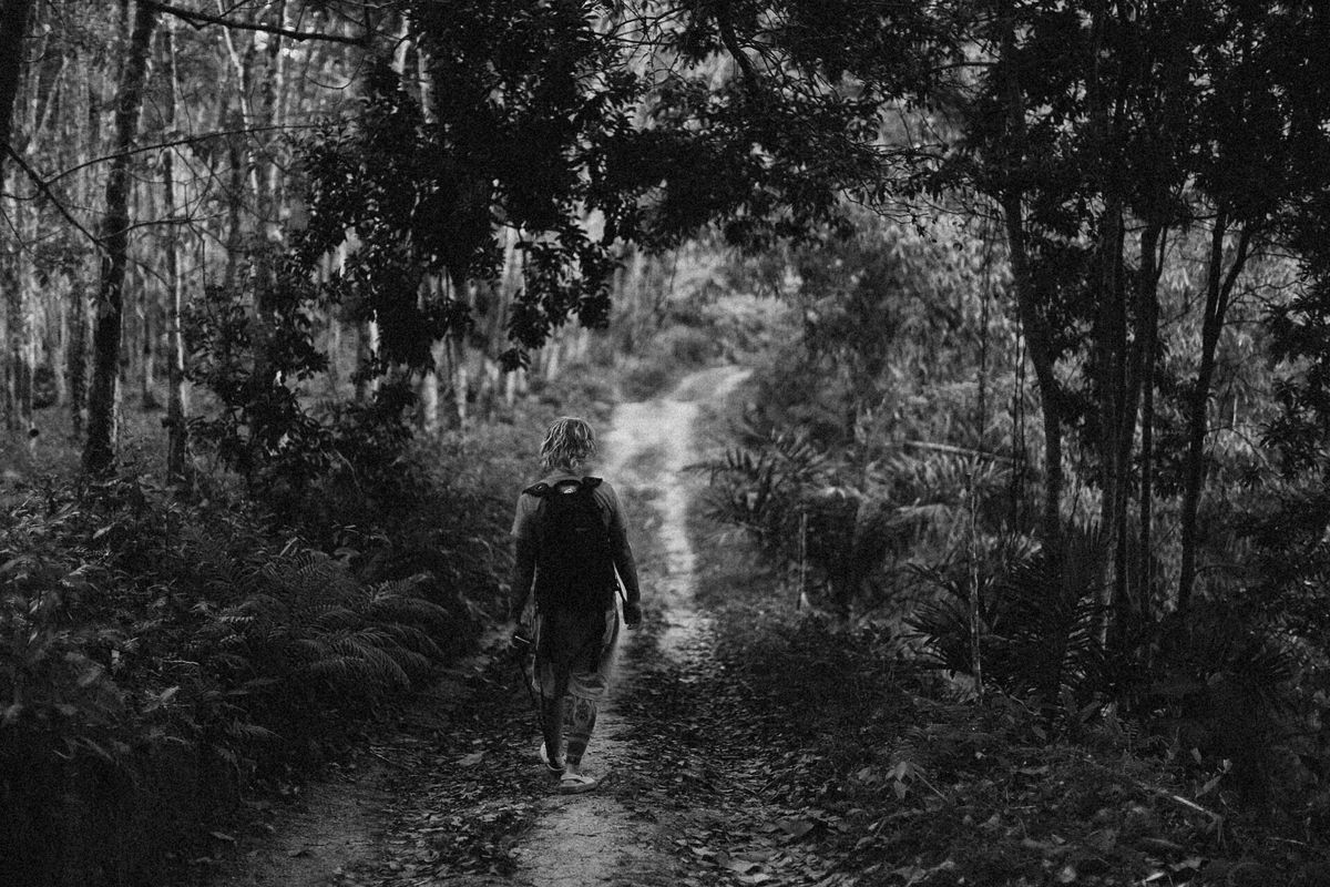 A person walks alone on a forest trail, captured in black and white, conveying solitude and nature. Illustrative editorial photograph.