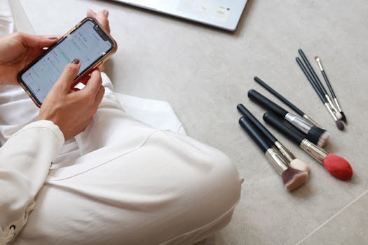 Woman using smartphone on floor beside makeup brushes in São Paulo.