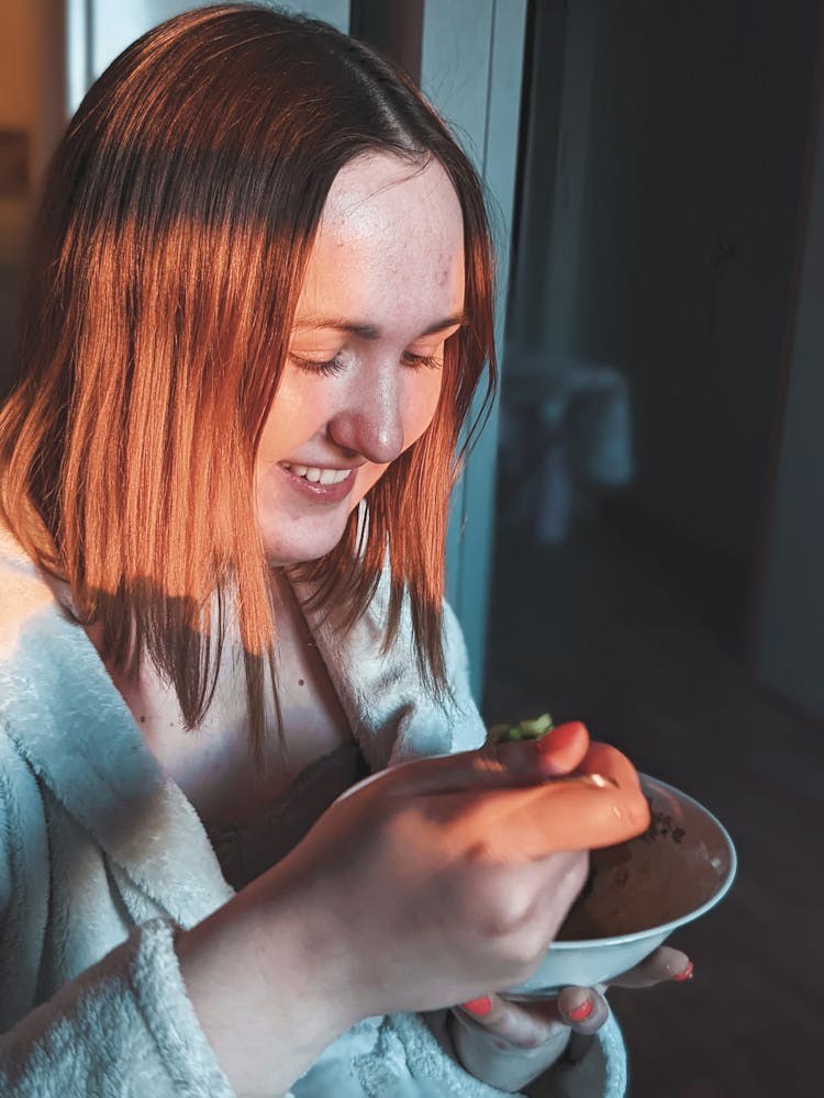 A Woman Looking At The Bowl Of Food She Is Holding