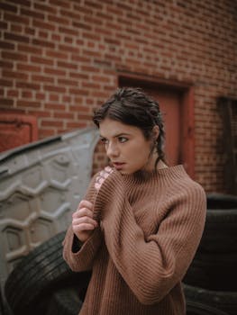 Woman wearing a brown sweater stands pensively against a brick wall in Des Moines, Iowa.
