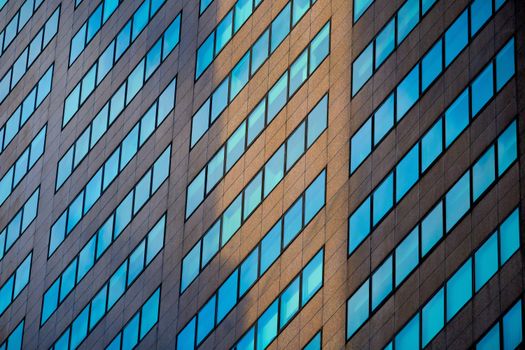 Low-angle view of a modern skyscraper with reflective glass windows creating a geometric pattern.