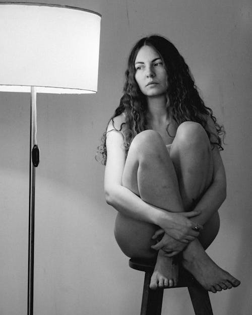 Grayscale Photo of a Naked Woman Sitting on a Stool