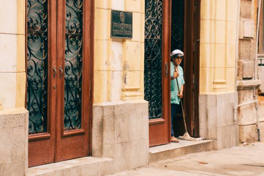 A person cleaning the entrance of a historic building with ornate doors, captured in an urban setting.